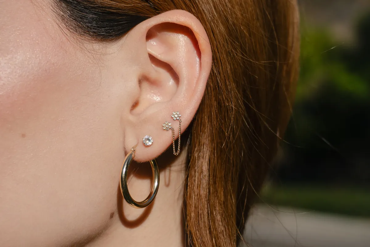 Close-up of an ear wearing a gold hoop and diamond stud earrings