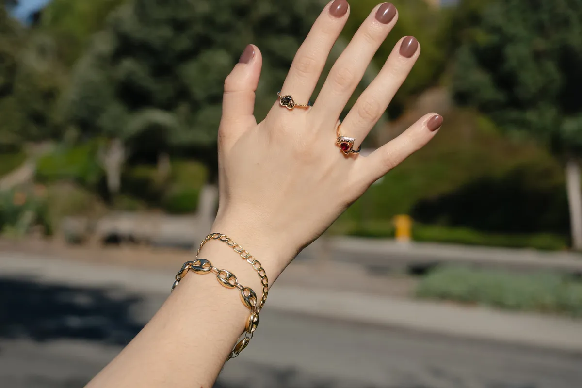 Hand raised showing gold rings and a chain-link bracelet