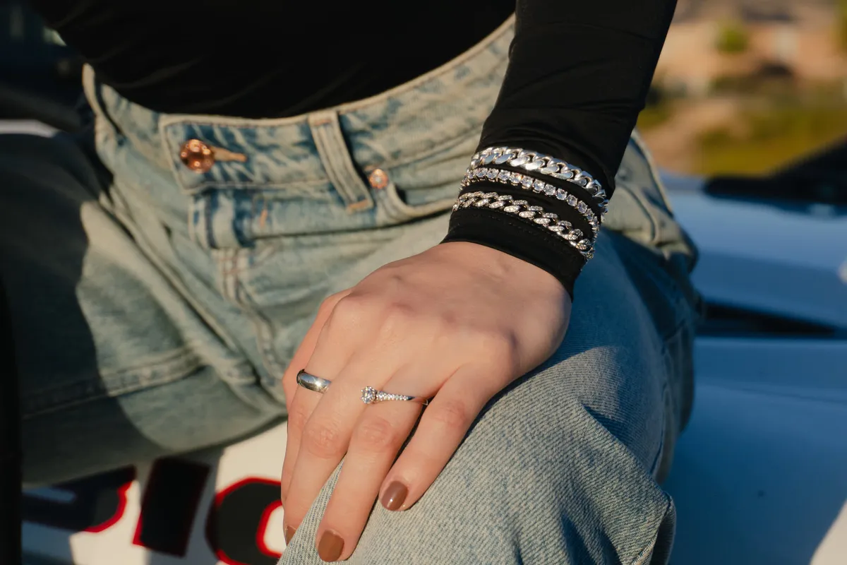 Hand resting on denim wearing a solitaire ring and stacked silver bracelets